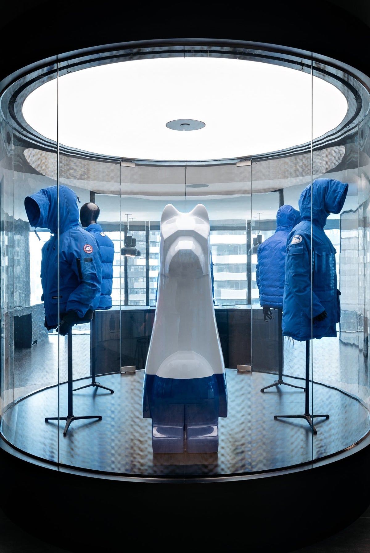 Blue parkas displayed on mannequins inside a circular glass display case.